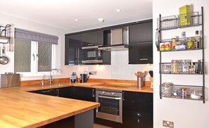A modern kitchen with black cabinets, stainless steel appliances, a wooden countertop, and a built-in oven.