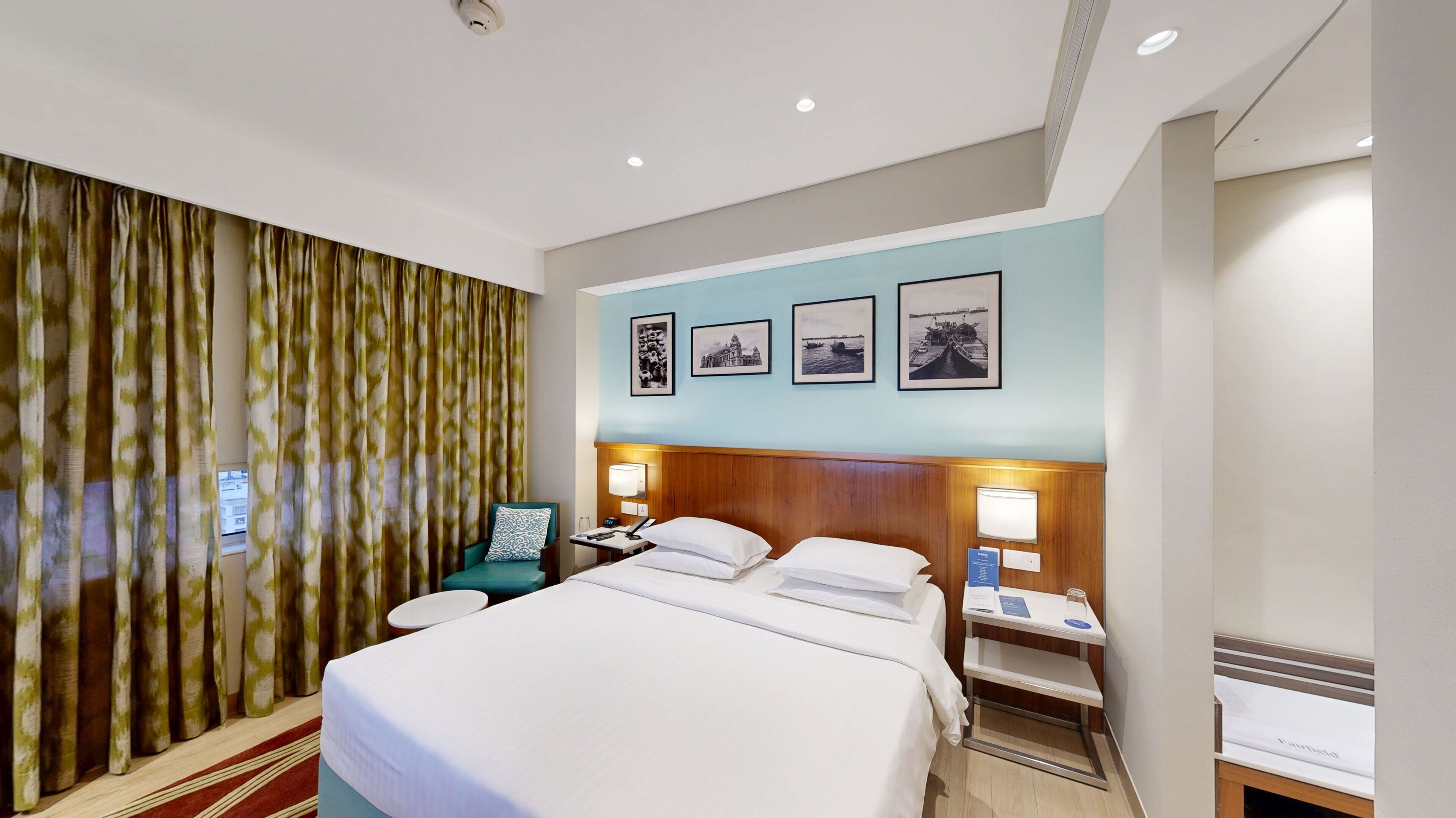 A hotel room with a bed, a nightstand, a chair, a desk, and a wall with framed pictures.