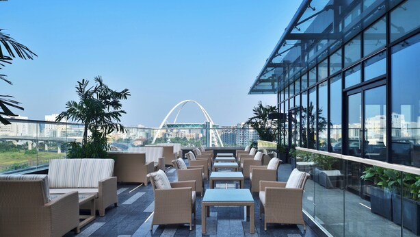 Terraza en la azotea con mobiliario de mimbre, barandillas de vidrio y vistas a un puente y el paisaje urbano.