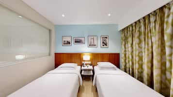 Habitación de hotel con dos camas, cabecero de madera, mesita de noche con lámpara, teléfono y cuadros en la pared.