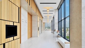 Un pasillo moderno con paneles de madera, un televisor de pantalla plana, un banco y ventanas amplias con vistas a la ciudad.