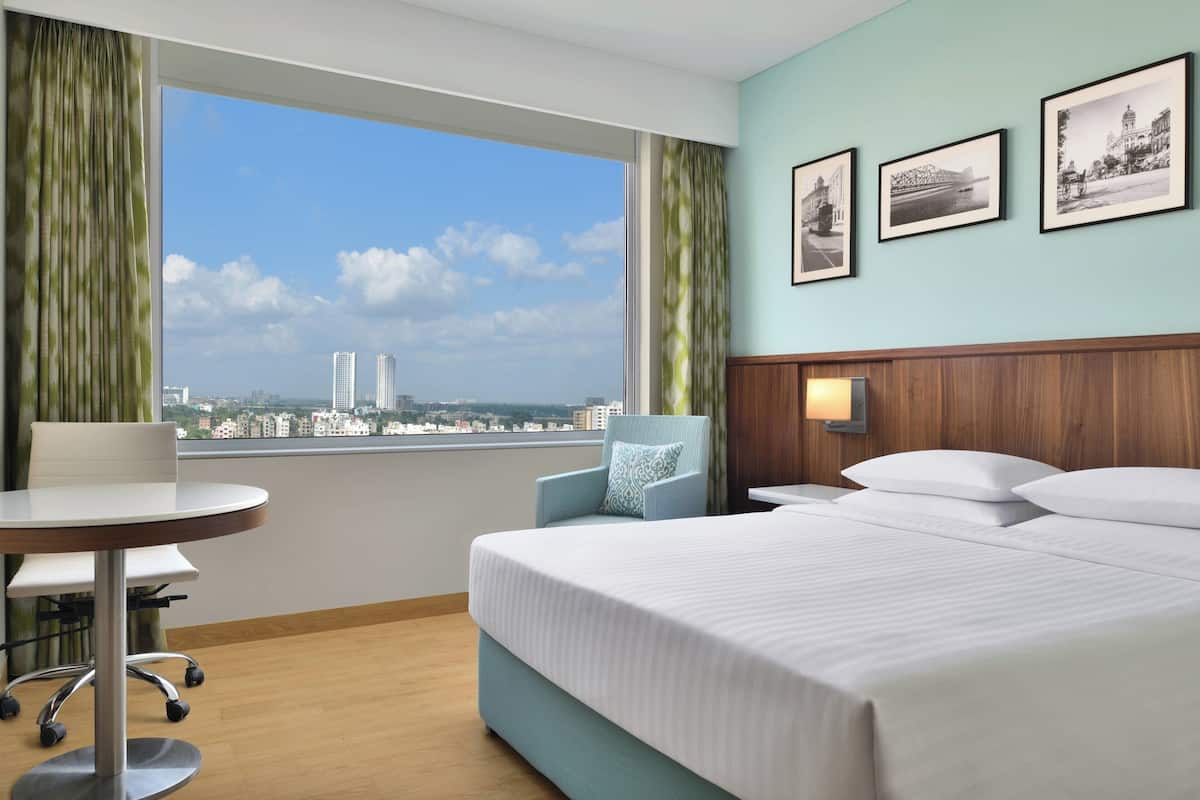 Habitación de hotel con un ventanal grande, una cama, un escritorio y una silla. Hay tres cuadros enmarcados en la pared.