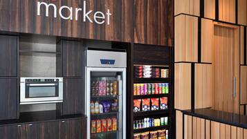 Un área de cocina con horno empotrado, refrigerador lleno de bebidas y estantes con aperitivos envasados.