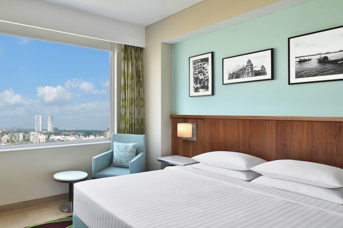 Habitación de hotel con una cama grande, una silla, una mesita y vistas a la ciudad a través de una ventana.