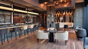 Un moderno bar con barra, taburetes y una zona de estar con mesas redondas y sillas.