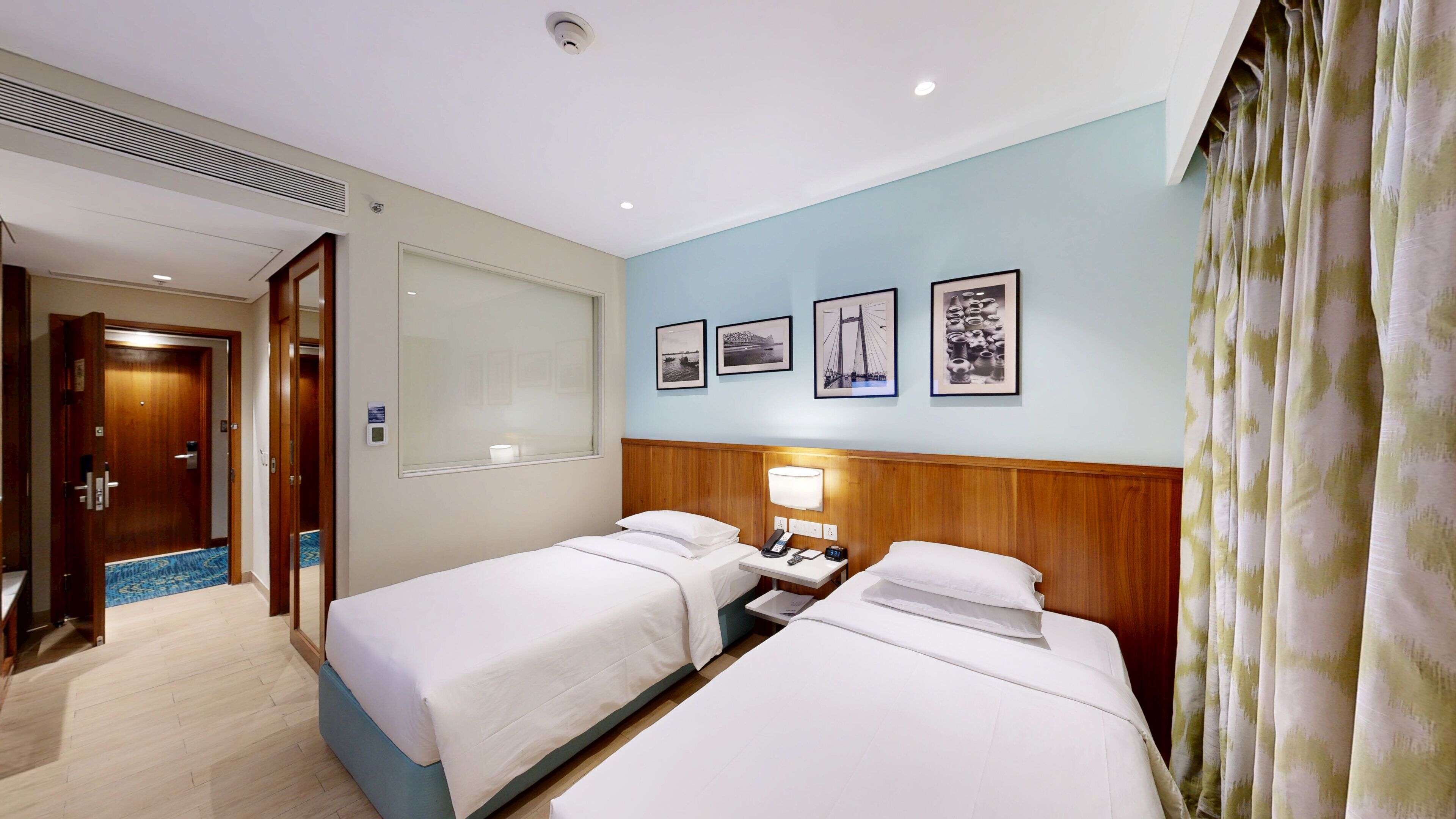 Ein Hotelzimmer mit zwei Betten, einem Nachttisch mit Lampe, einem an der Wand befestigten Telefon und gerahmten Bildern.