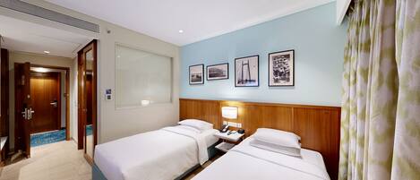 A hotel room with two beds, a bedside table with a lamp, a wall-mounted phone, and framed pictures.