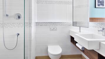Un baño moderno con ducha envuelta en vidrio, inodoro blanco y tocador con espejo.
