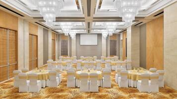 Un salón de conferencias con mesas redondas, sillas blancas y candelabros.