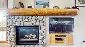 A stone fireplace with a TV mounted above it, a wooden shelf with decorative items, and a wooden cabinet below the TV. - Snowcreek V 999 Mammoth Mountain Views, Private Washer Dryer, Pet-Friendly by RedAwning (Mammoth Lakes)