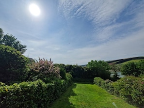 A well-maintained garden with a clear pathway leading to a body of water, surrounded by lush greenery and trees.
