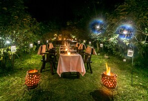 An outdoor dining area with a table set for two, surrounded by chairs, and two decorative pottery lamps on stands. - Amakoro Songa Lodge (Nyange)