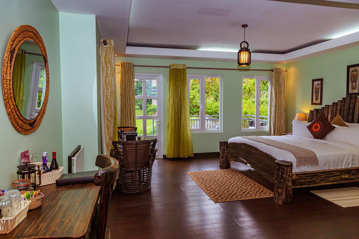 A bedroom with a wooden bed, a dining table with chairs, a mirror, and a window with curtains.
