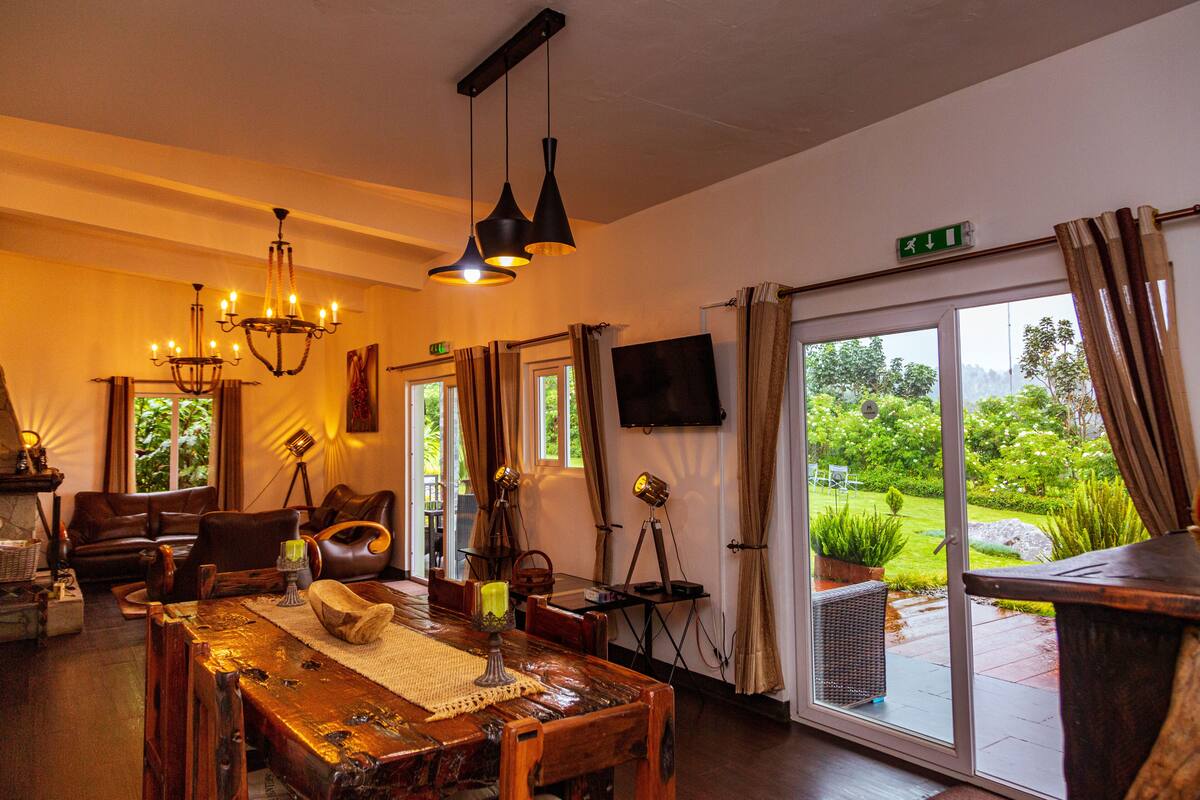 A spacious room with a wooden dining table, leather seating, and a large window offering a view of greenery.