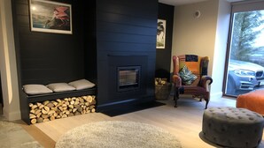 Una sala de estar moderna con chimenea, un tapete redondo y una zona de estar con una silla y reposapiés.