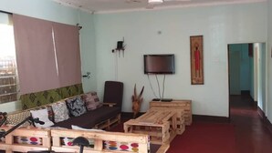 Uma sala de estar com sofá, mesas de madeira, televisão e obras de arte nas paredes.