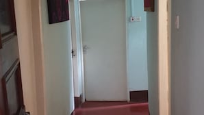 Um corredor com piso vermelho, paredes azul claras e uma porta branca no final.