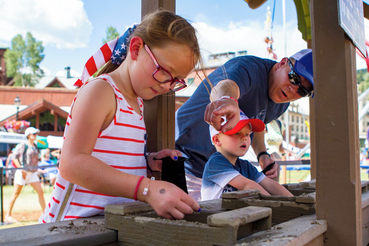 A child and an adult working on a wooden structure, possibly a playhouse, outdoors.