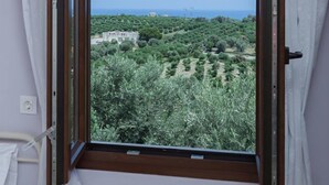 A room with a window overlooking a landscape with trees and a view of the sea. - Mela Villas (Rethymno)