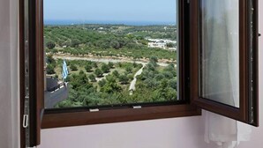 A room with a large window overlooking a green landscape and a clear sky. - Mela Villas (Rethymno)