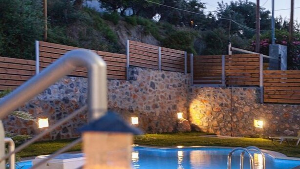 A swimming pool with a stone wall and wooden fence in the background. - Mela Villas (Rethymno)