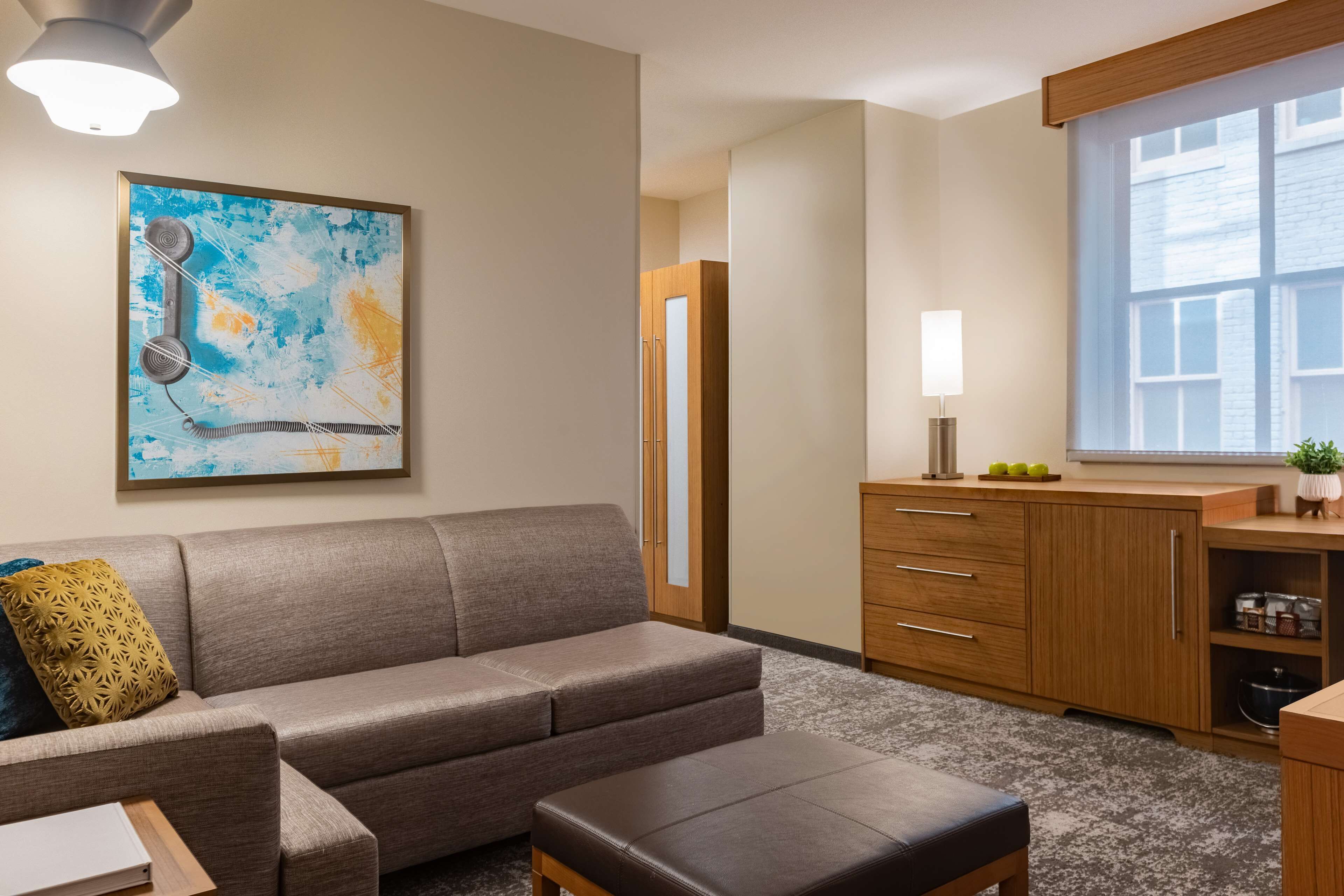 A modern living room with a sofa, ottoman, and a painting on the wall.