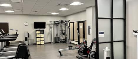 A gym with treadmills, weight machines, and a wall-mounted TV.