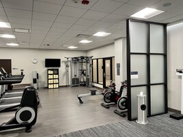 Un gimnasio con cintas de correr, máquinas de pesas y un televisor montado en la pared.