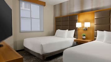 Une chambre d’hôtel avec deux lits, une télévision, une fenêtre et une table de chevet avec une lampe et une plante.
