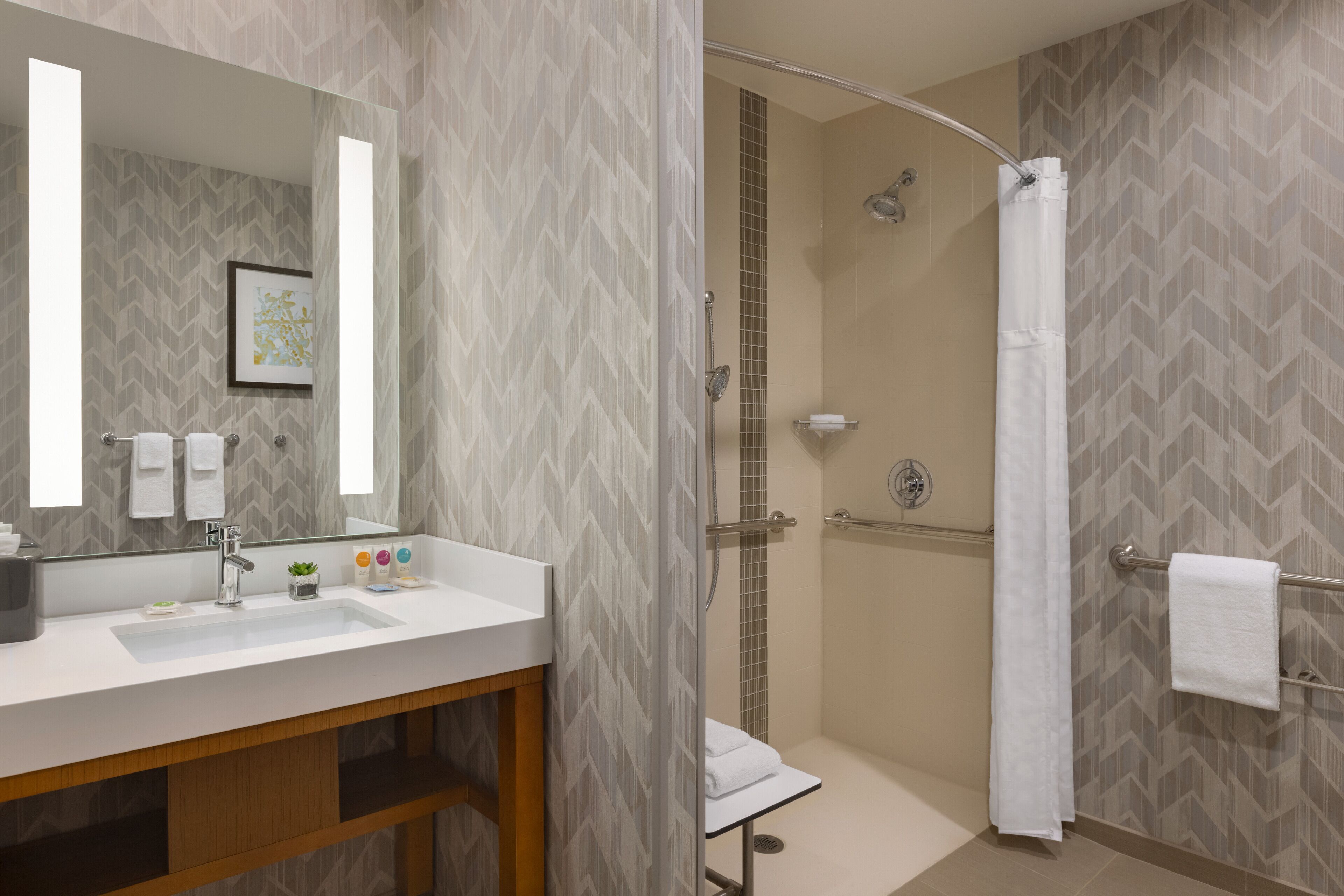 A modern bathroom with a large mirror, a sink, a shower with a glass door, and a towel rack.