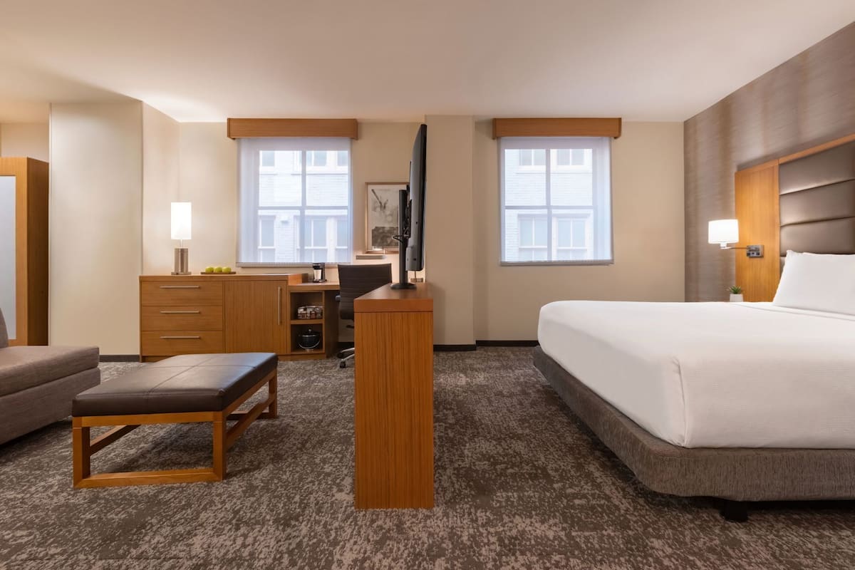 A hotel room with a bed, a desk, a chair, a TV, and a lamp.
