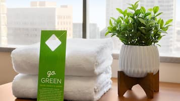 Una pila de toallas blancas con una tarjeta verde que dice “go GREEN” junto a una planta en maceta sobre una mesa de madera.