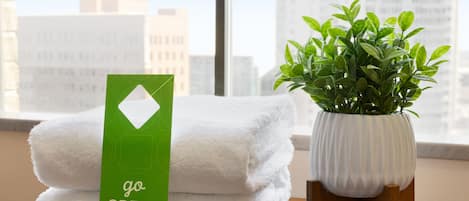 A stack of white towels with a green card labeled "go GREEN" beside a potted plant on a wooden table.