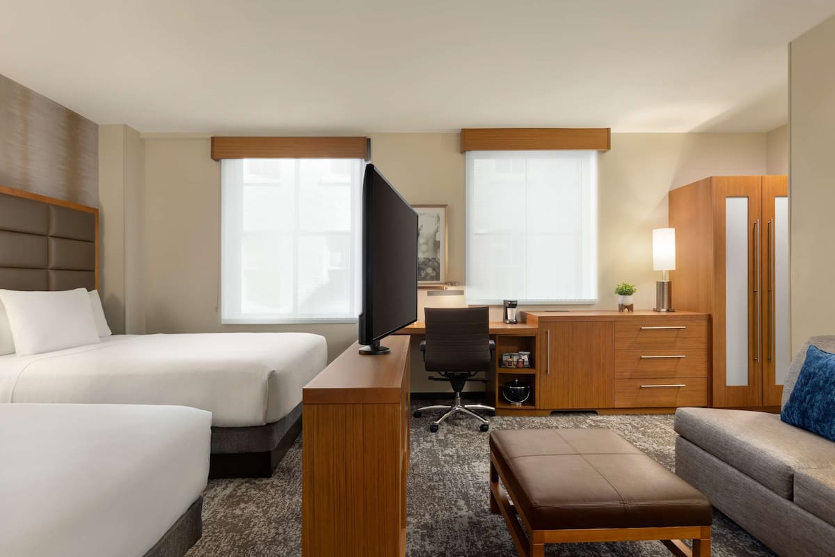 A hotel room with two beds, a desk with a computer, a chair, a sofa, and a TV.