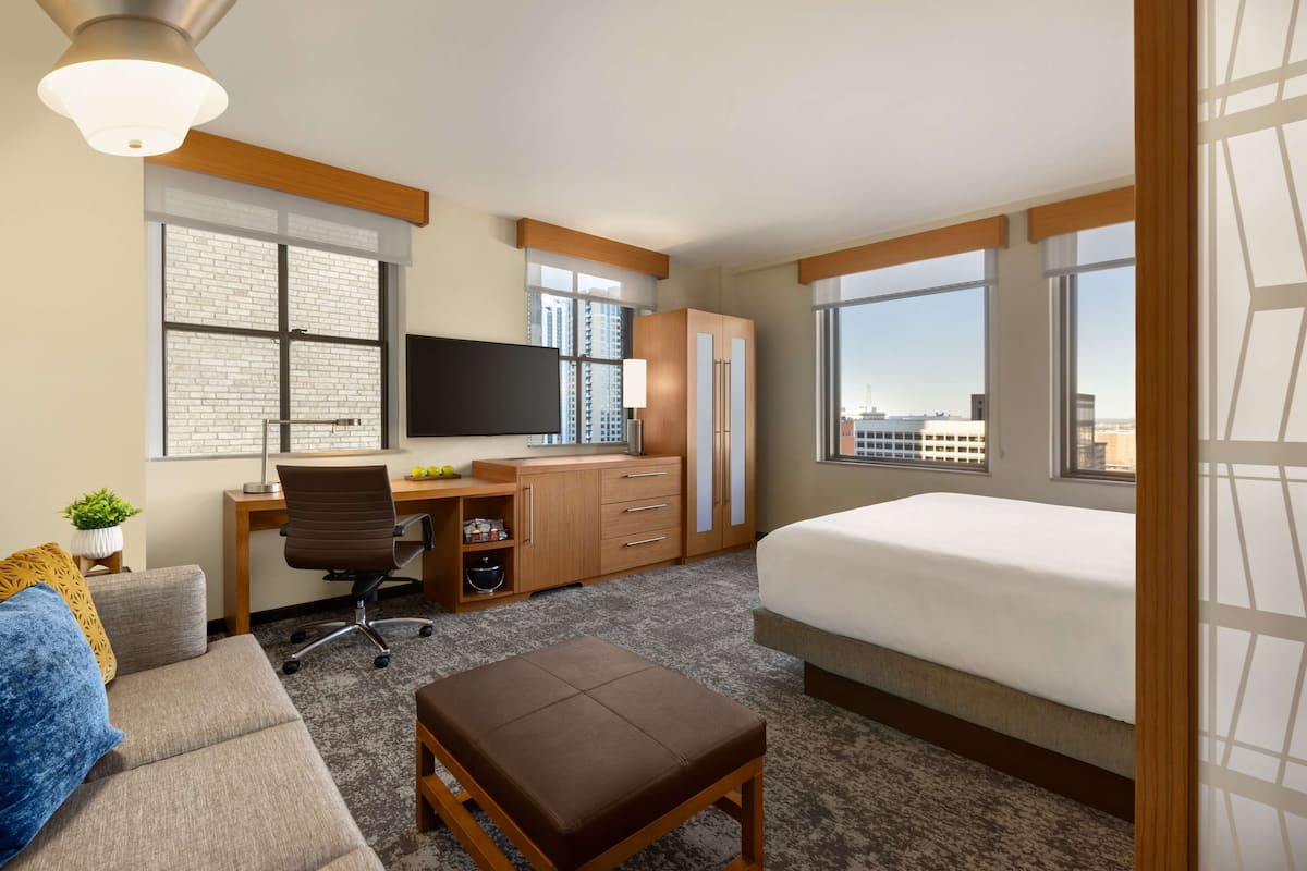 A hotel room with a bed, a desk with a chair, a TV, and a window with a city view.