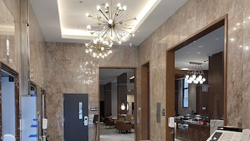 A modern hotel lobby with marble walls, a central chandelier, and a reception desk.