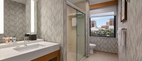 A modern bathroom with a large mirror, a glass-enclosed shower, and a view of buildings through a window.