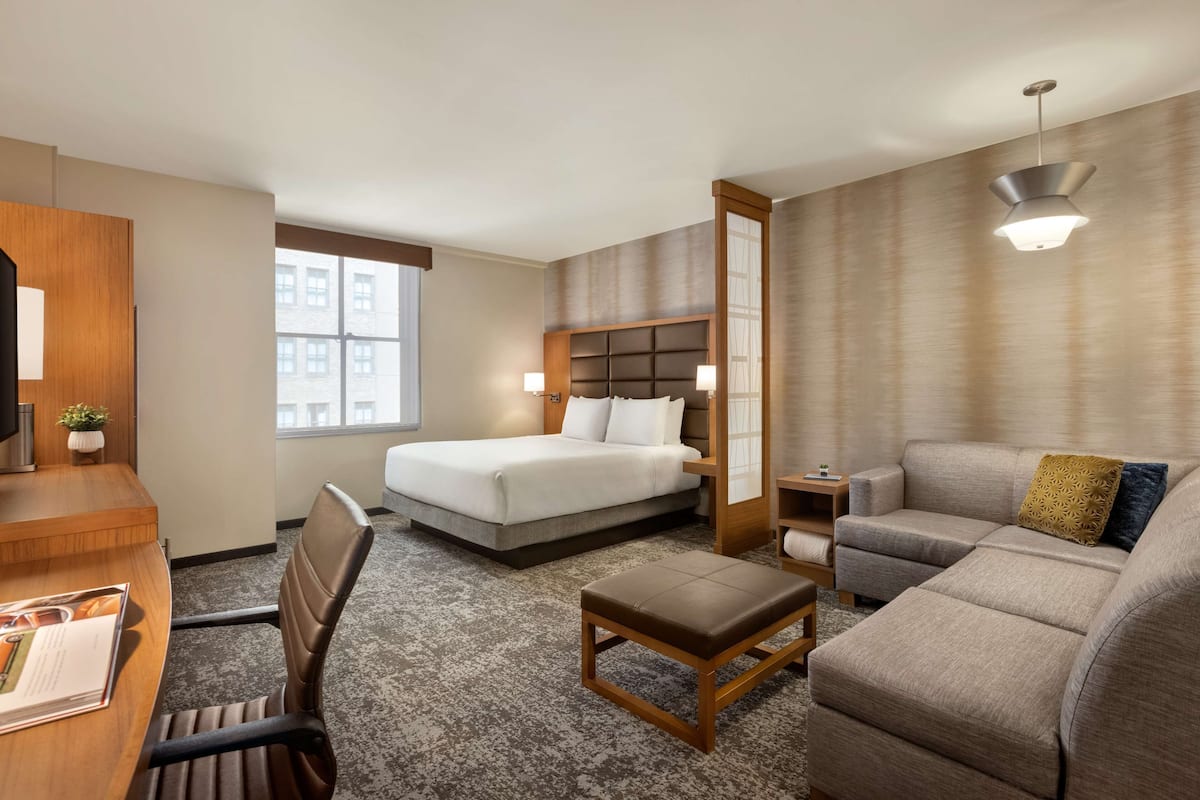 A hotel room with a bed, a sofa, a desk, and a chair.