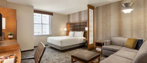 A hotel room with a bed, a sofa, a desk, and a chair.