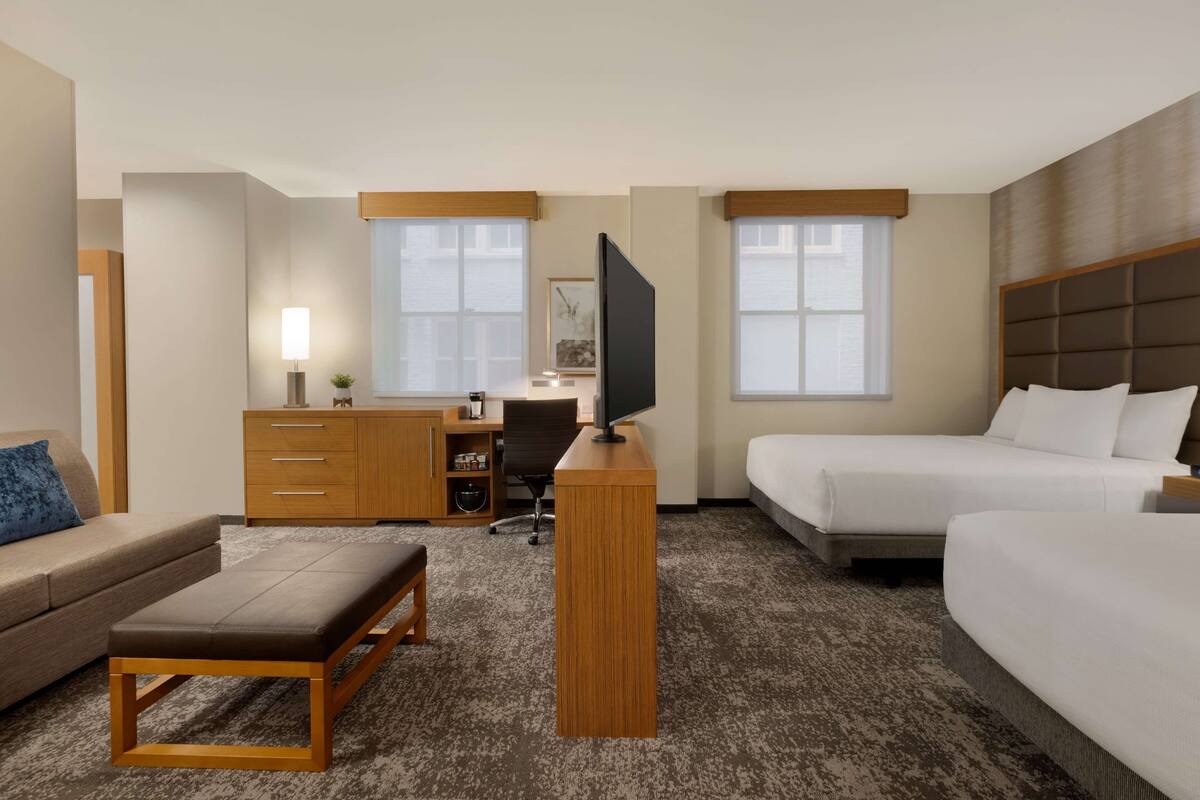 A hotel room with a bed, a desk, a chair, a sofa, a bench, and a TV.