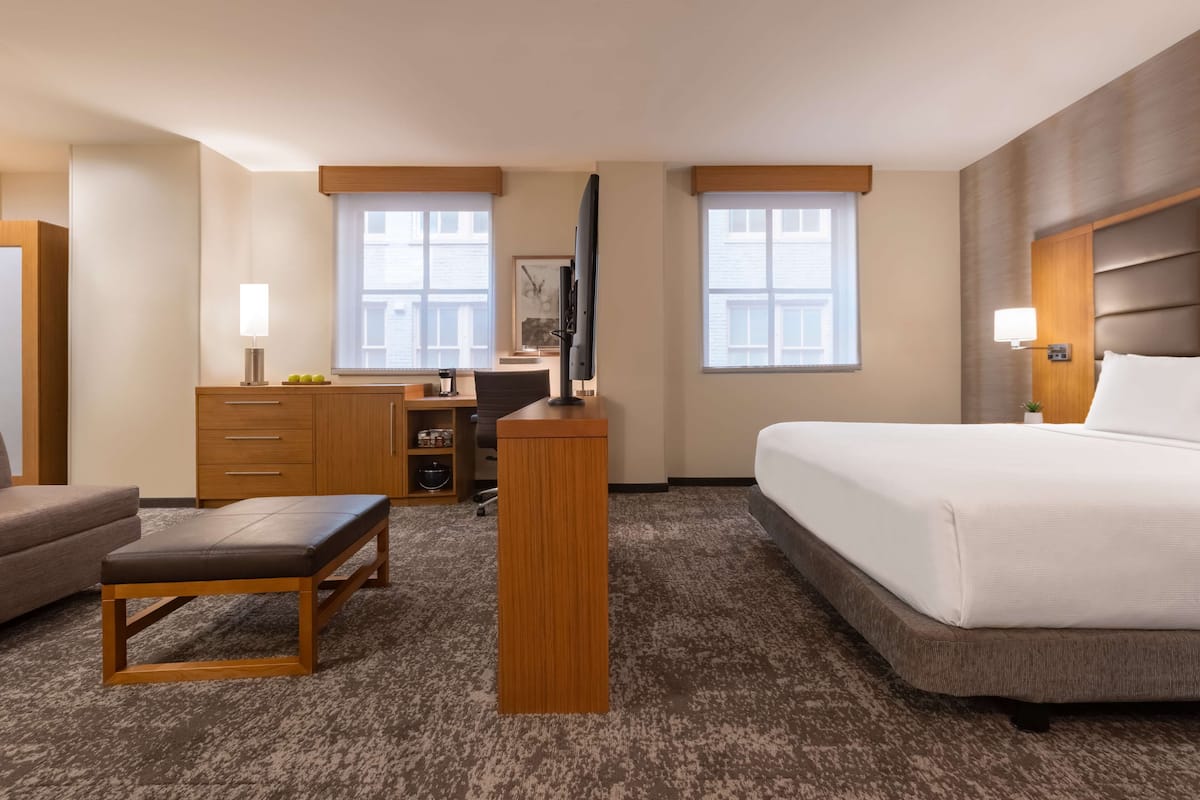 A hotel room with a bed, a desk with a computer, a chair, a small table, and a sofa.