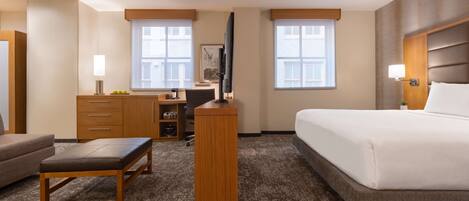 A hotel room with a bed, a desk with a computer, a chair, a small table, and a sofa.