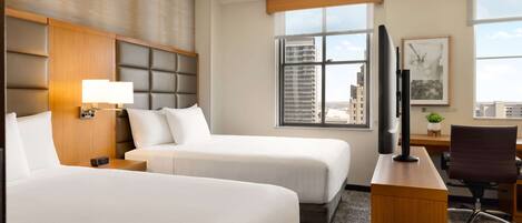 A hotel room with two beds, a desk, a television, and a window with a city view.