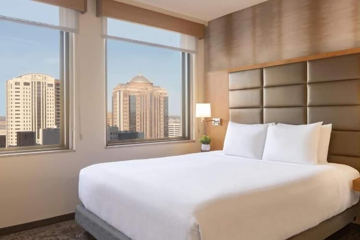A hotel room with a large bed, a city view, a padded headboard, and bedside lamps.