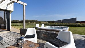 An outdoor deck with a hot tub, two white chairs, a table with a coffee pot, and a stone wall. - Villa Frouden, Beach, sea view, jacuzzi (Plouescat)