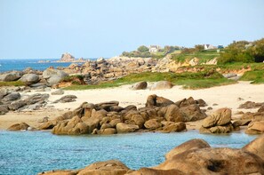 A rocky beach with large boulders, a sandy shore, and a building in the background.