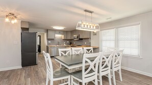 Una cocina moderna con armarios grises, un refrigerador negro y un comedor con mesa de madera y sillas blancas.