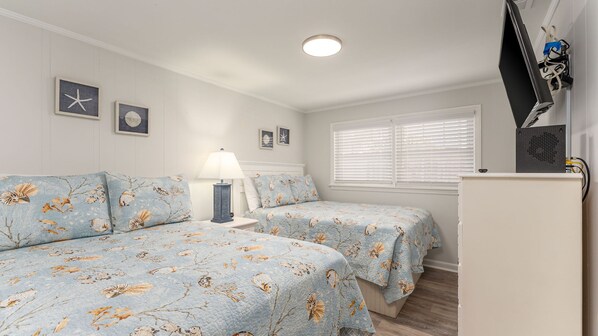 A bedroom with two beds, a nightstand, a lamp, a TV, and a window with blinds.