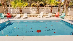 Una piscina con sillones de descanso y una valla de madera al fondo.