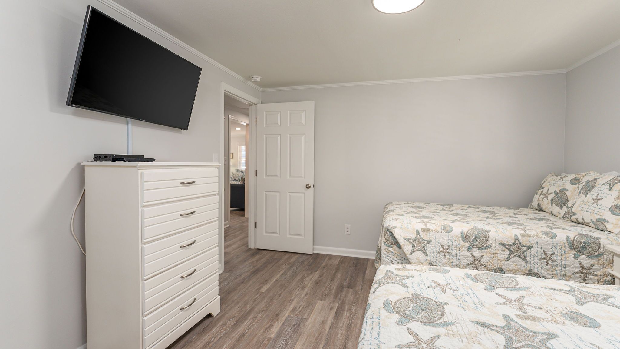 Een slaapkamer met een bed, een dressoir, een televisie en een deur naar een andere kamer.